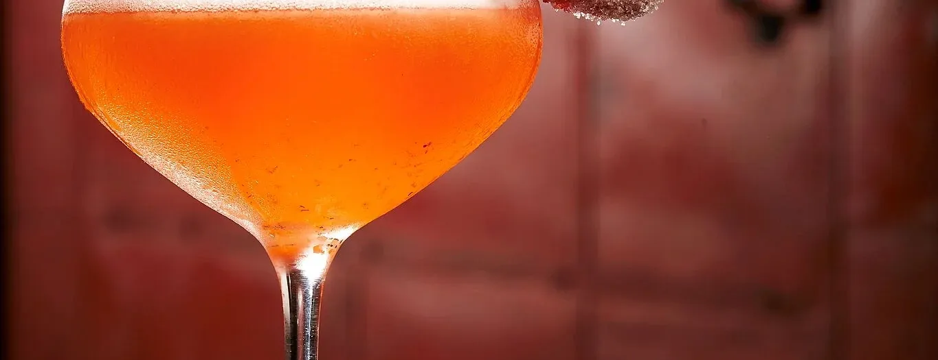 A strawberry cocktail served up in a coupe, rimmed with a sugared strawberry