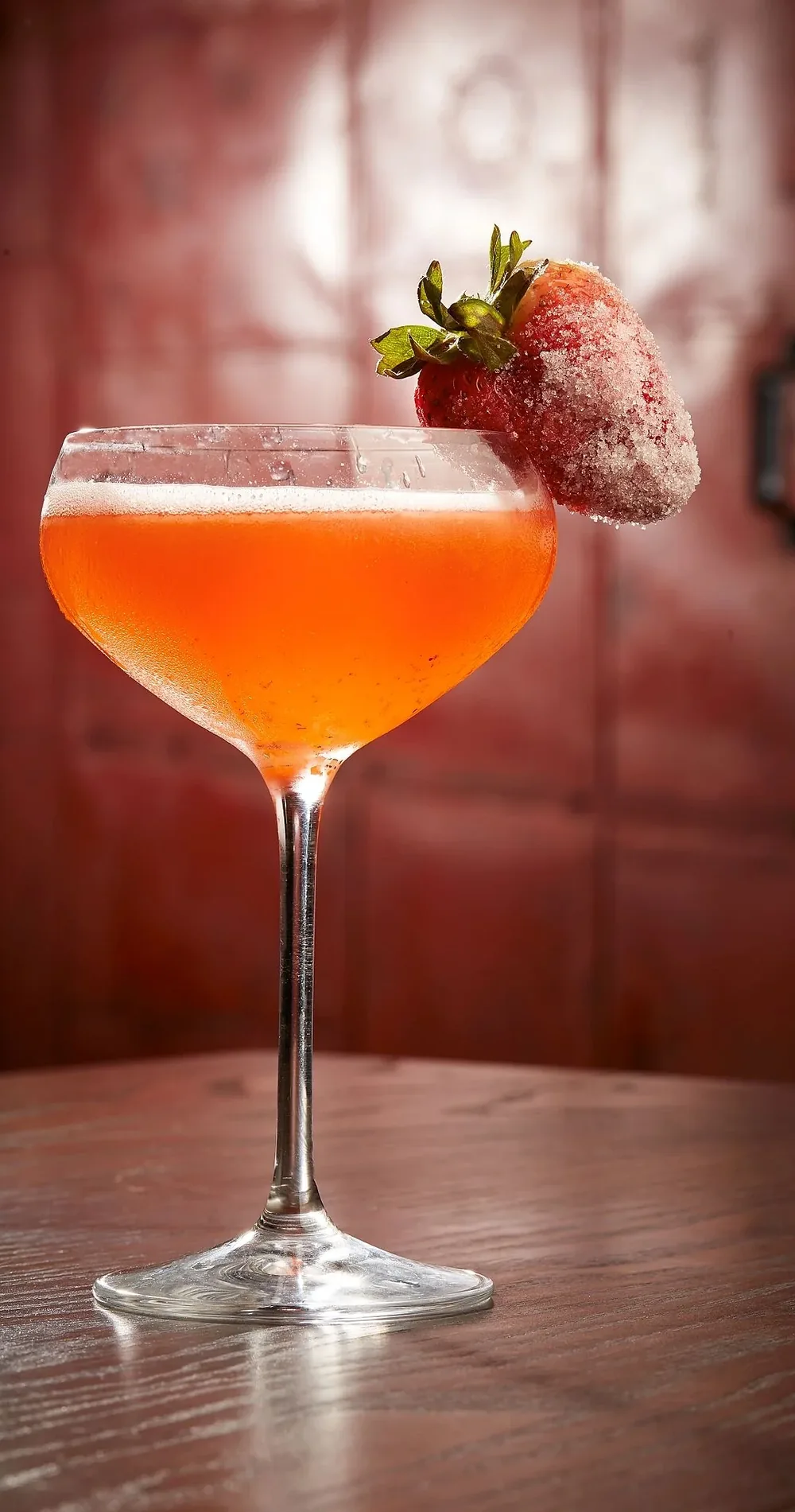 A strawberry cocktail in a coupe glass with a sugared strawberry on the rim